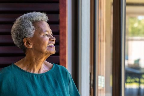 Senior african american woman looking out sliding door smiling peaceful home portrait