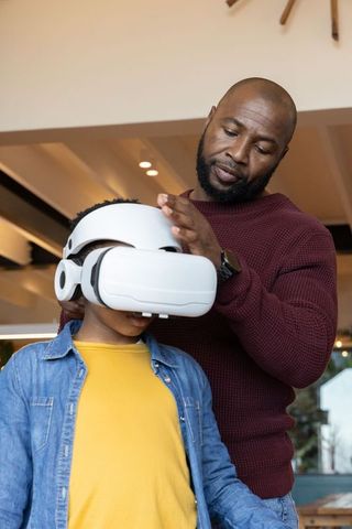 African American father adjusting VR headset on son, encouraging home learning and bonding