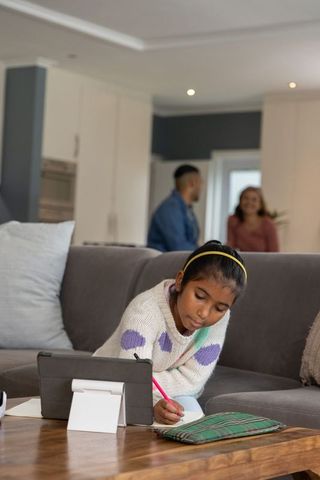 Indian girl studying at home with tablet and notebook on living room coffee table