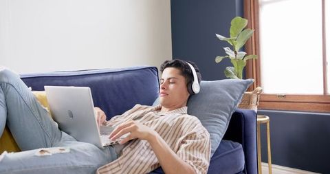 Young Man on Couch Relaxed Using Laptop and Headphones