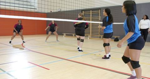 Multicultural high school volleyball team competing indoors wearing knee pads