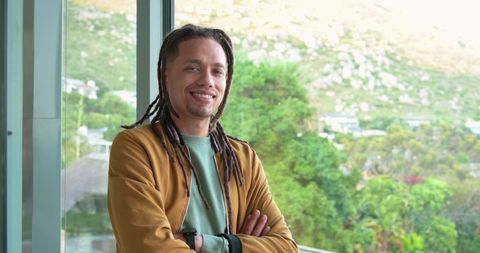 Smiling mid adult man with dreadlocks leaning on balcony overlooking green hillside