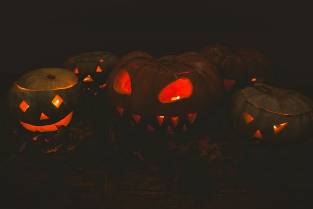 Illuminated jack-o'-lanterns with various facial expressions glowing in a dark room. Perfect for Halloween-themed decorations, party invitations, and festive social media posts. Ideal for creating a spooky atmosphere in advertisements, blogs, and websites related to Halloween celebrations.