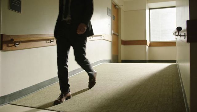 Businessman walking through sunlit corporate corridor with wooden handrails, doorway light