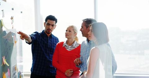 Pointing leader guiding team brainstorming at glass wall with colorful sticky notes
