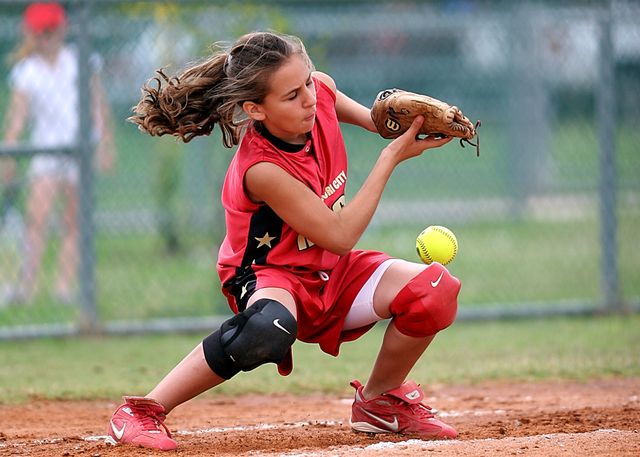 Young female athlete intensely focused on catching ball in action-packed softball game. Example of dedication, athleticism, girl power, and youth sports. Ideal for use on sports websites, children's sports promotion, advertisements for sports equipment, and inspiring youth participation in sports.