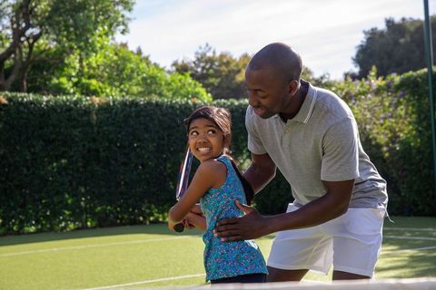 Father Guiding Daughter in Tennis on Grass Court