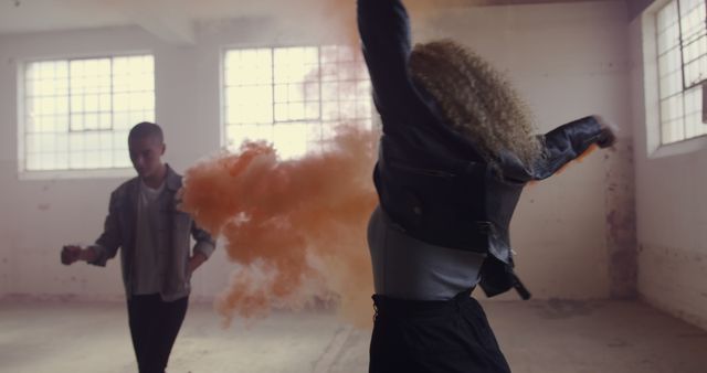 Young hip-hop dancers perform energetically with vibrant orange smoke in an industrial-style space filled with natural light. Suitable for use in urban culture projects, dance workshops, creative advertisements, and youth-oriented campaigns emphasizing artistic expression and dynamic movement.