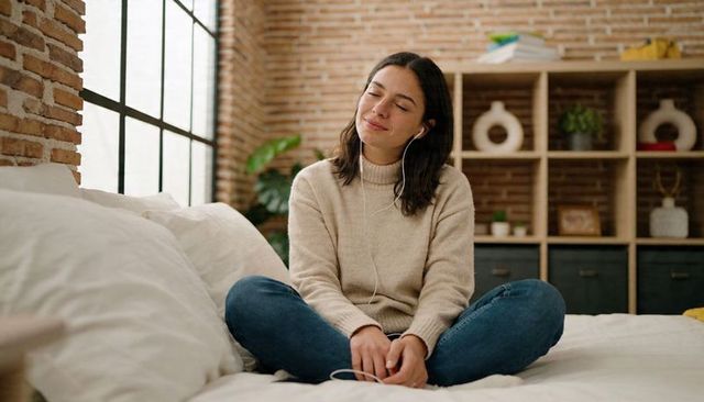 Woman relaxing on bed listening to music with earbuds in cozy loft bedroom