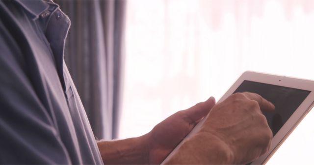 Close-up of man using tablet at home near window - Download Free Stock Images Pikwizard.com