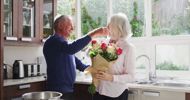 Senior man giving a bouquet of flowers to his wife and hugging her in the kitchen at home. social distancing quarantine lockdown during coronavirus pandemic