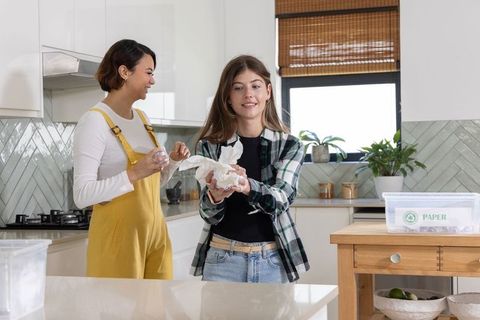 Diverse women sorting paper recycling in bright modern kitchen promoting sustainability