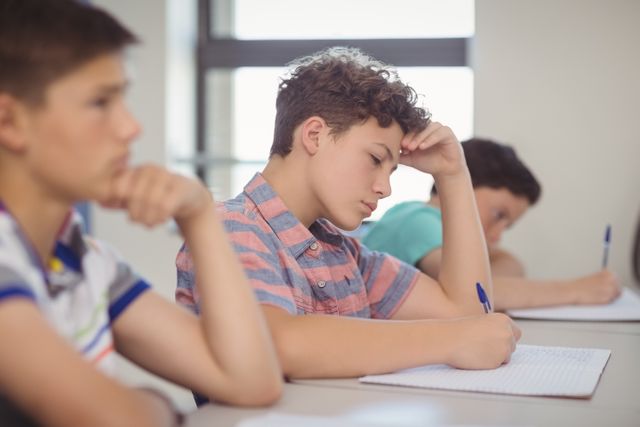 Boys are concentrating on their studies, writing in notebooks during a classroom session. Ideal for educational content, school brochures, academic articles, and learning resources.
