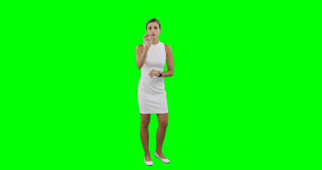 This image shows a businesswoman wearing a white dress standing on a green screen background. She is analyzing or pointing towards something, possibly making a presentation. Ideal for use in professional or corporate contexts, marketing materials, or business presentations.