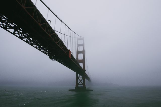 Golden Gate Bridge disappearing into thick fog over San Francisco Bay. Ideal for travel magazines, articles on San Francisco, weather effects, and architecture reviews.