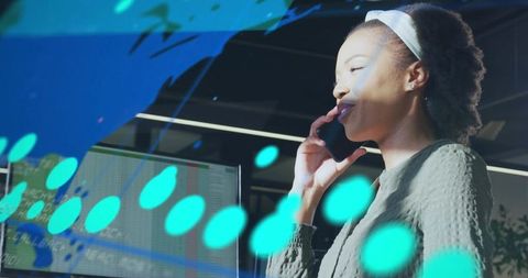 Professional woman talking on smartphone while monitoring financial charts on office display