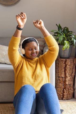 African american woman relaxing at home listening to music and stretching in cozy mustard sweater