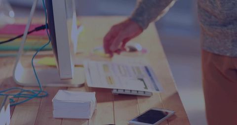 Man Reaching for Spreadsheet on Minimalist Desk with Computer, Smartphone and Notes