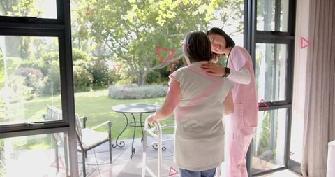 Caregiver Supporting Senior Woman Using Walker at Sliding Door with Sunlit Garden View