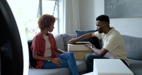 Unboxing at home by African man and African American woman in modern living room on gray sofa