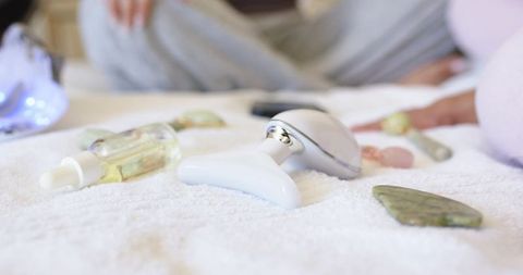 Diverse women relaxing on towel using t-shaped facial gua sha and handheld silver massager