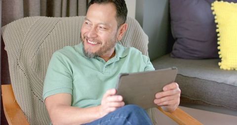 Mature Asian Man Relaxing with Tablet in Cozy Living Room