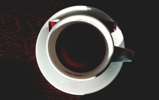 This image shows a top view of a cup of coffee on a wooden table. The cozy chiaroscuro highlights the ambiance, perfect for uses in coffee shops, blogs about morning routines, caffeine articles, or social media posts about enjoying coffee.