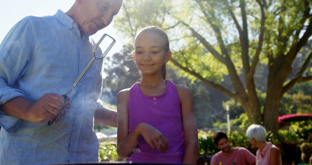 Grandfather and Granddaughter Barbecuing in Park with Family - Download Free Stock Images Pikwizard.com