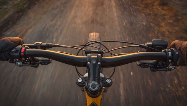 Pov mountain biking gripping handlebars on sunlit gravel trail with knobby tire motion