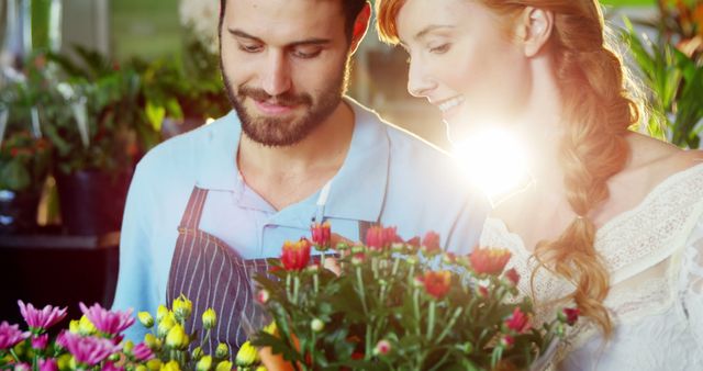 This image showcases a couple happily selecting flowers in a bright, sunlit flower shop. Ideal for use in advertisements, blogs, or articles related to gardening, relationships, joy, and floral businesses. The warm sunlight adds a serene and inviting atmosphere.