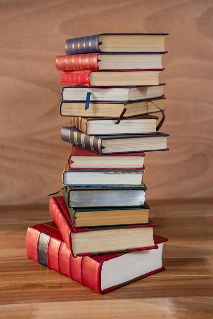 This image shows a tall stack of various books placed on a wooden table. Ideal for use in educational materials, library promotions, reading campaigns, and academic websites. It conveys themes of knowledge, learning, and literature.