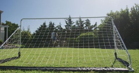 African american father and son playing soccer in sunny backyard with portable goal