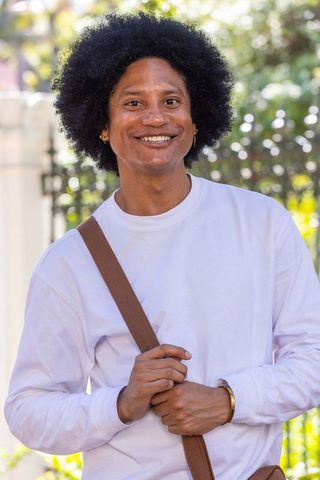 Smiling african american man wearing white shirt holding brown crossbody strap outdoors