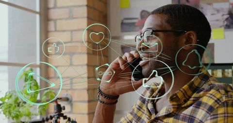 Young man talking on phone with social media icons overlay in creative office workspace