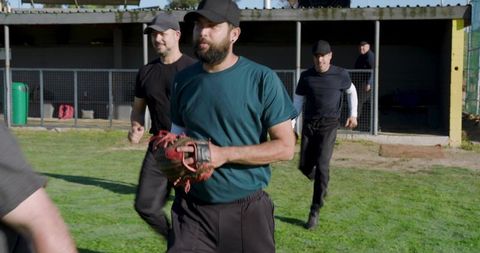 Diverse male baseball teammates running toward camera holding red glove in dugout practice