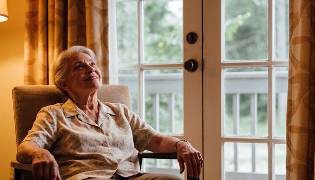 Senior woman relaxing in armchair by french doors, gazing upward, peaceful home moment