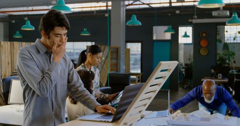 Young Man Contemplates Solution in Modern Office with Colleagues