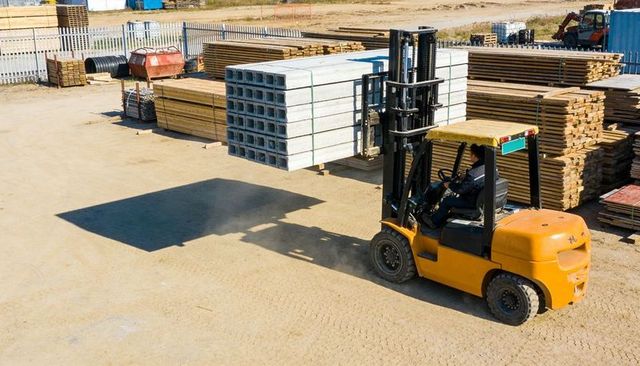Yellow forklift lifting precast hollowcore slabs and stacking lumber at construction supply yard