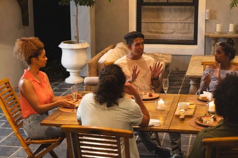 Friends gathering on patio for casual evening dining while man gestures in conversation