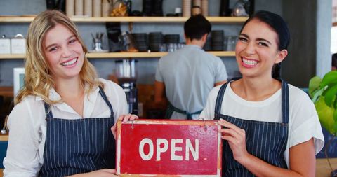 Smiling waitstaff holding open sign in cafe