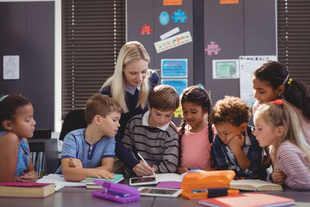Teacher helping a diverse group of elementary students with their homework in a classroom. Ideal for educational content, school-related articles, and teaching resources. Highlights teamwork, collaboration, and the importance of academic support.