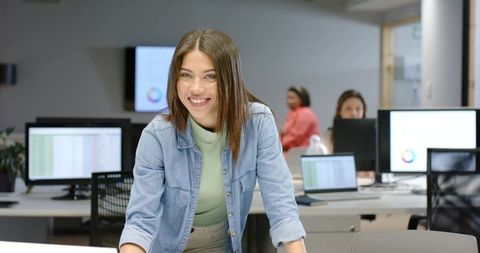 Indian woman leaning on desk smiling in modern office teamwork productivity collaboration scene