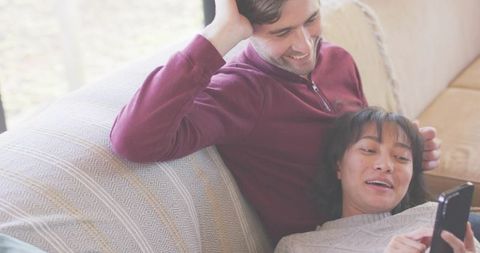 Couple relaxing on patterned couch while woman showing smartphone to partner in living room