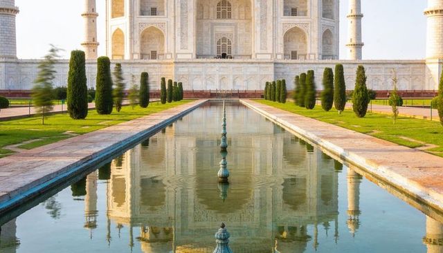 White marble mausoleum reflecting in central pool of mughal charbagh garden at golden hour