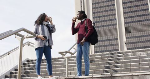 Diverse coworkers drinking coffee and checking smartphone on urban office steps