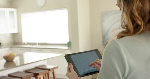 Woman using tablet to control smart home devices in bright modern kitchen, home automation