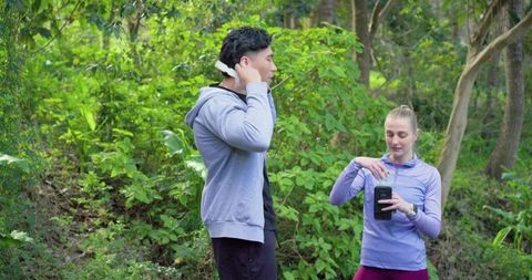 Runners pausing on forest trail checking phone and hydration while adjusting headphones