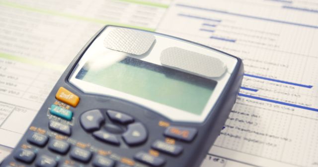 Detailed close-up of a calculator resting on a desk with financial documents. Suitable for illustrating concepts related to finance, accounting, or business analysis. Ideal for use in materials about financial planning, budgeting, or statistical analysis.