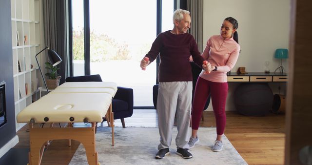 Senior man engaging in physical therapy exercises with assistance from a professional therapist in a home environment. Useful for themes related to senior health, rehabilitation, elderly care, and wellness programs. Could be used in promotional materials for physical therapists, healthcare providers, or senior living communities.