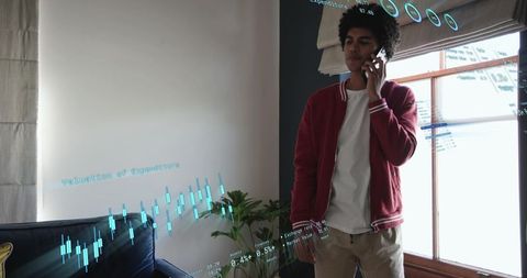 Young man talking on phone while viewing augmented reality financial data in living room